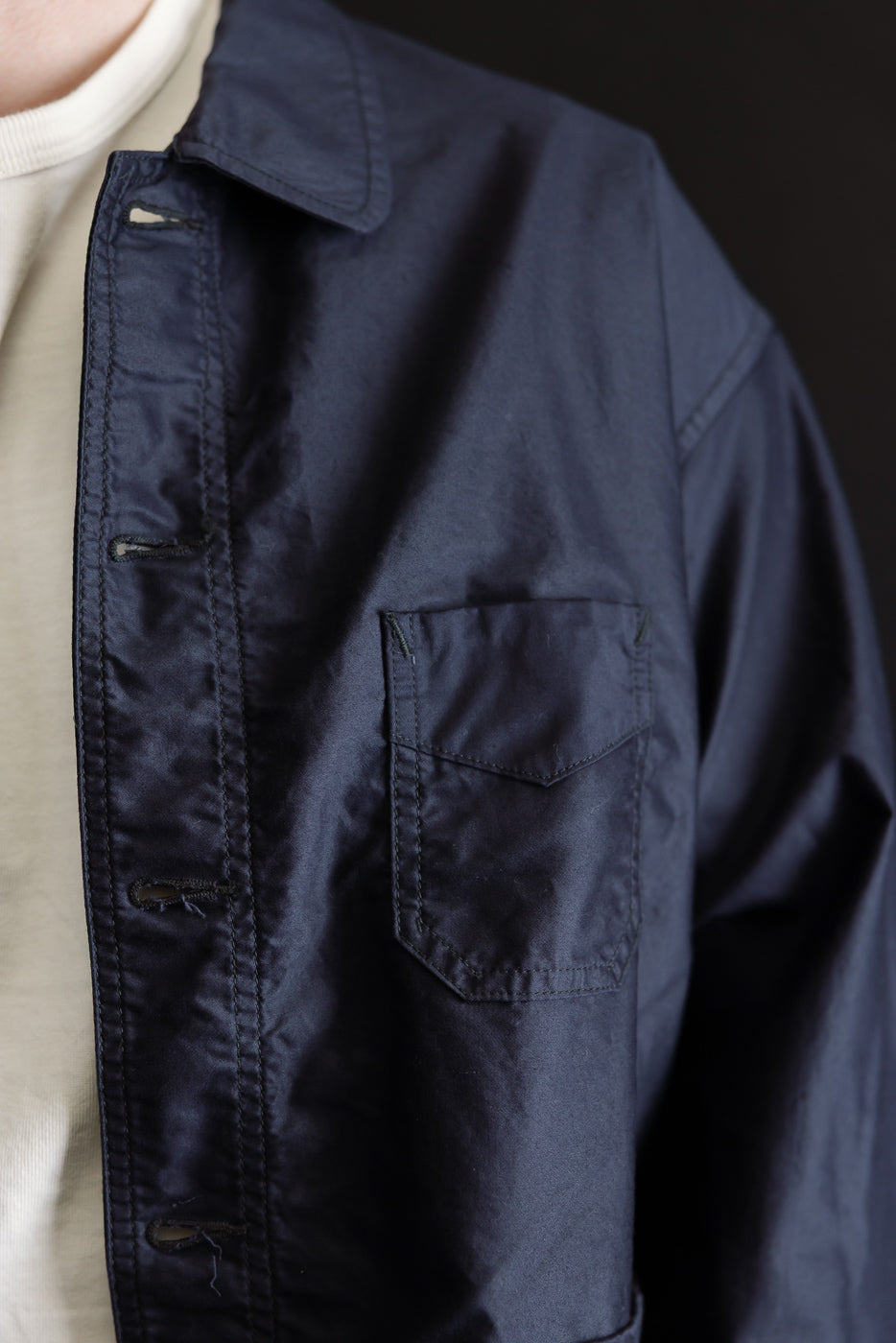 Close-up of the 3135-LMN - Post Chinois Travail 2 Light Moleskin jacket in dark navy, showcasing its cropped length, flap pocket, buttonholes, and meticulous stitching over a cream t-shirt.