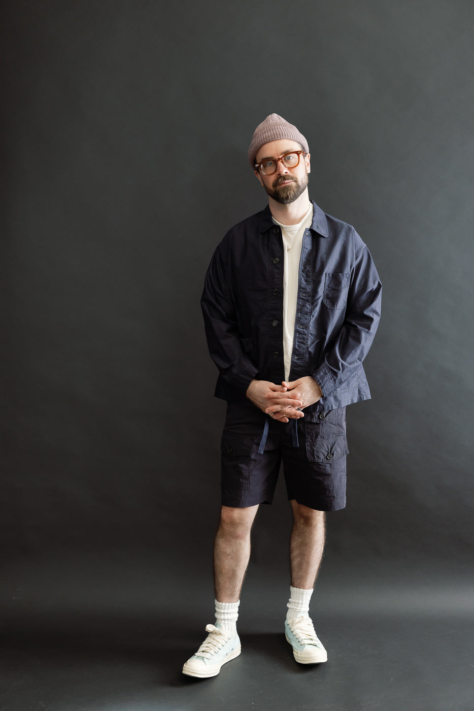 A man models the 3135-LMN - Post Chinois Travail 2 Light Moleskin - Dk. Navy, showcasing its cropped fit, rounded collar, and relaxed silhouette over a casual ensemble including a white T-shirt and navy shorts.