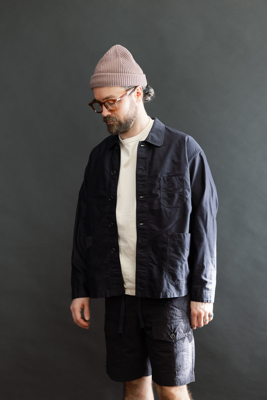 Man in 3135-LMN - Post Chinois Travail 2 Light Moleskin jacket, dark navy, with chore-style design, layered over a white T-shirt. Paired with matching cargo shorts, showcasing a relaxed, utilitarian weekend look.