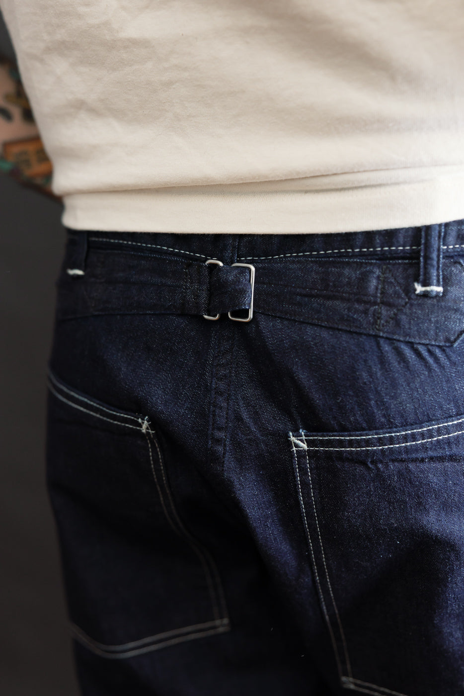 Close-up of the back of dark indigo denim pants on male model 5'9, 165lbs, showing cinch strap and pocket stitching.