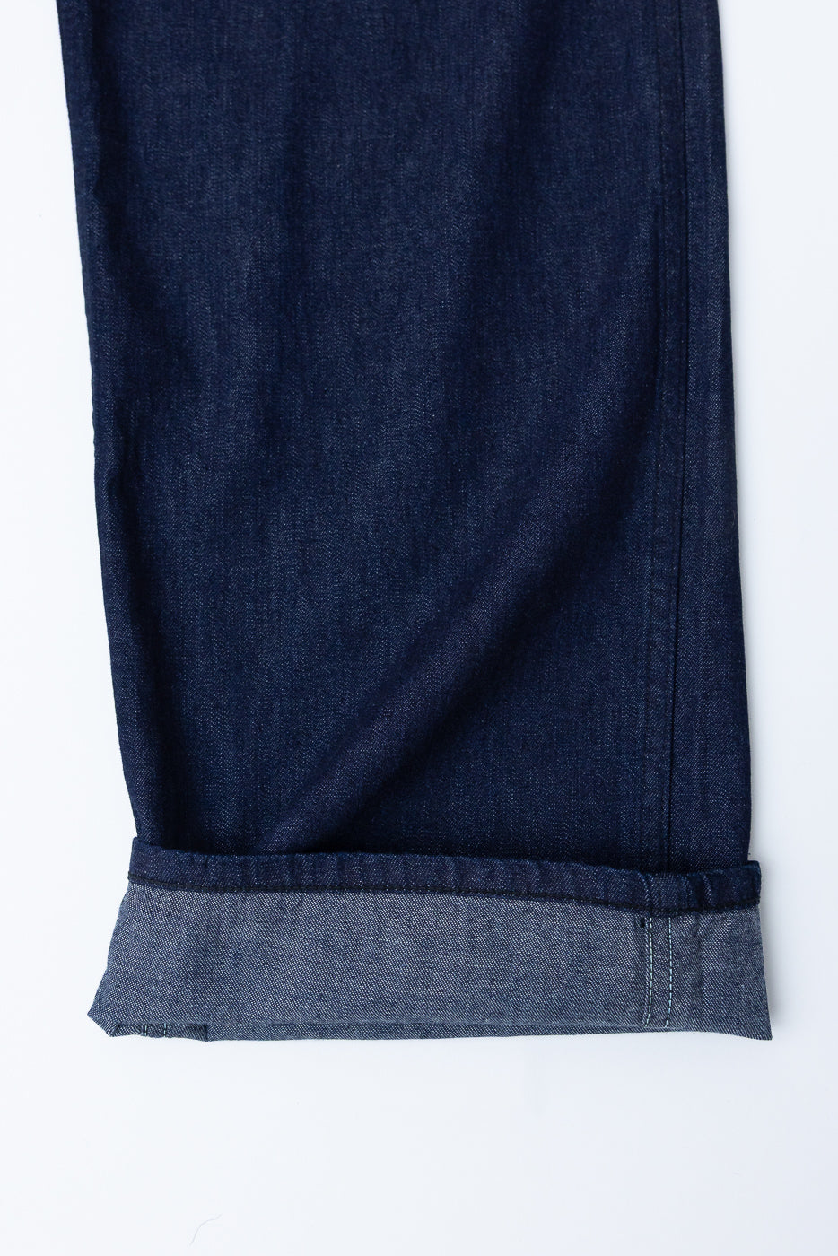 Close-up of front lower leg and cuff of dark indigo denim pants, showing fabric texture and hem detail.