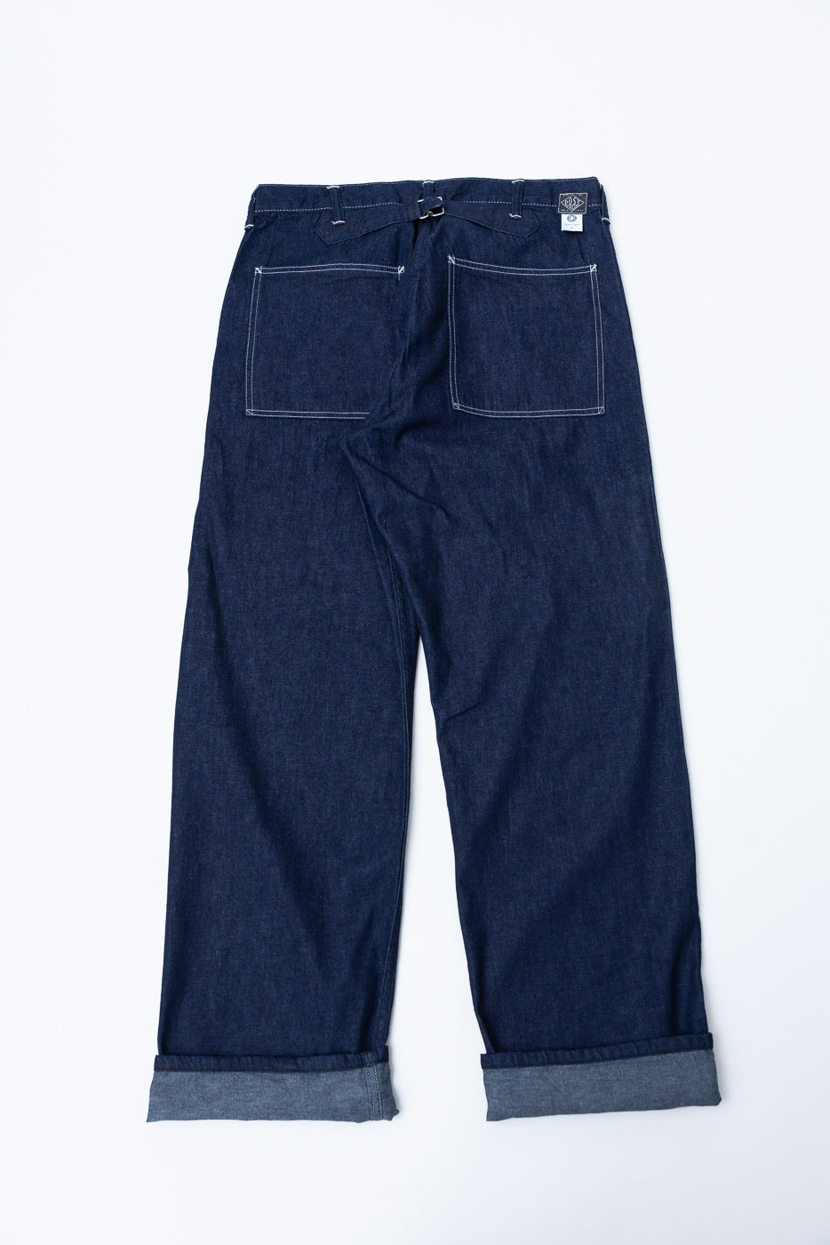 Flat lay, back view of dark indigo denim pants showing rear pockets, cinch, and rolled cuffs.