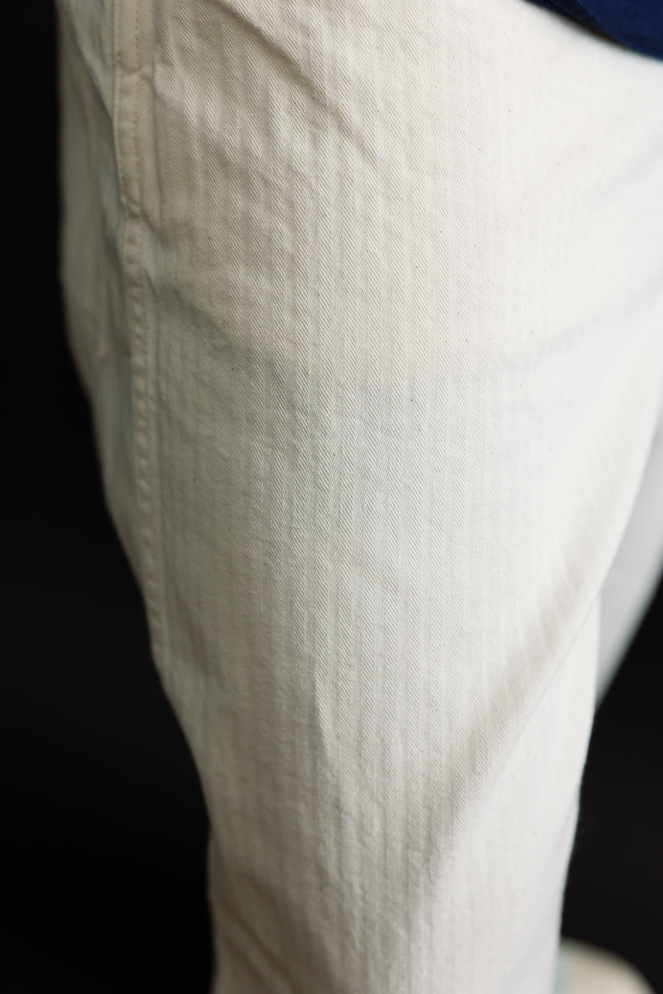 Close-up of the left front thigh on natural herringbone twill pants, showing fabric texture.