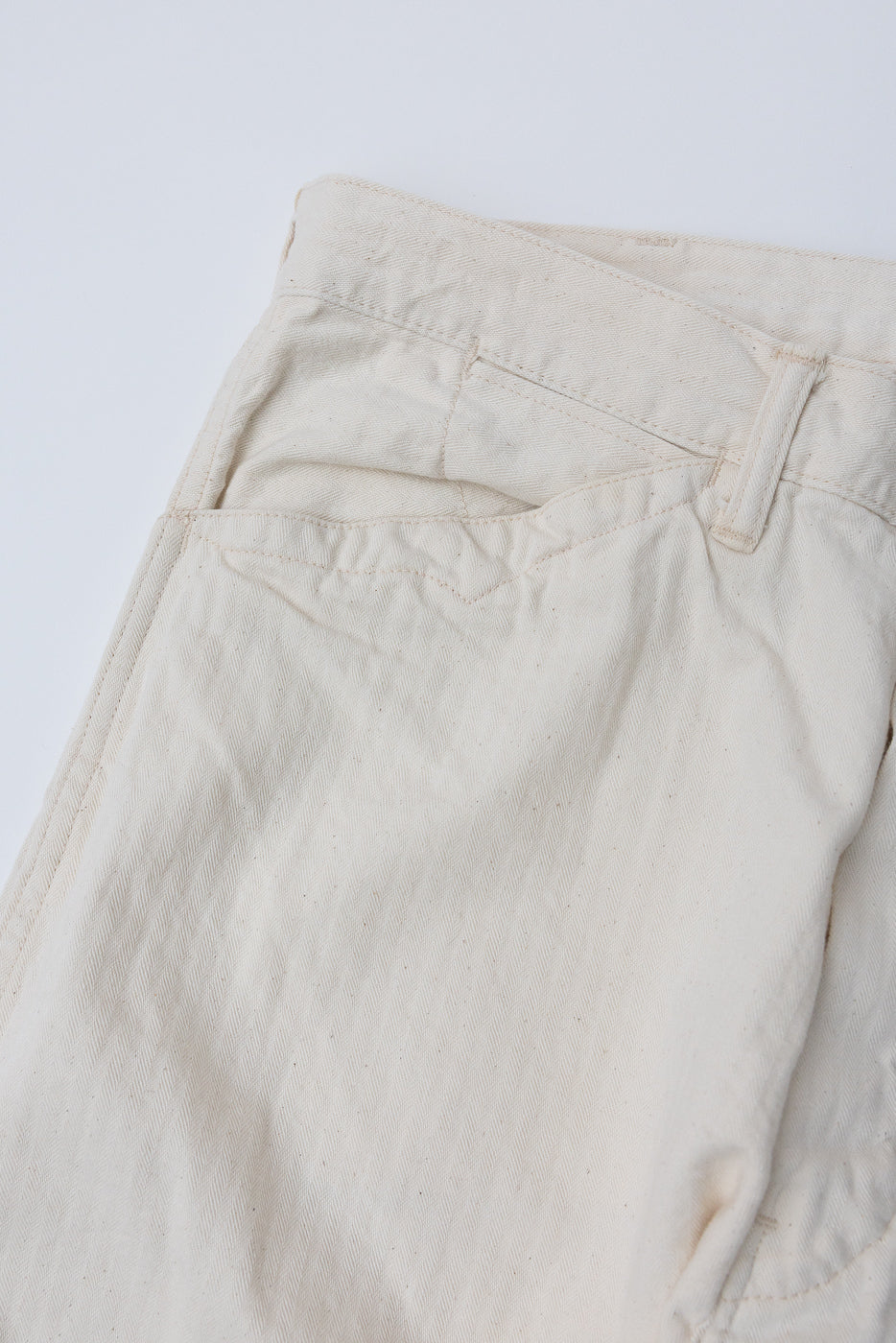 Close-up of natural herringbone twill pants, flat lay, back side showing rear pocket and belt loop detail.