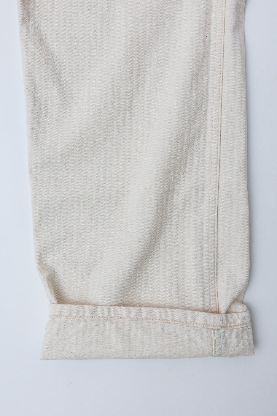 Close-up of pant leg hem, showing natural herringbone fabric and side seam detail, flat lay front view.