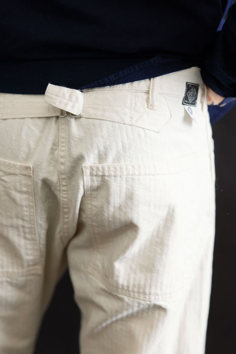 Close-up rear view of natural color herringbone pants, back pockets, belt loop detail on male model 5'9