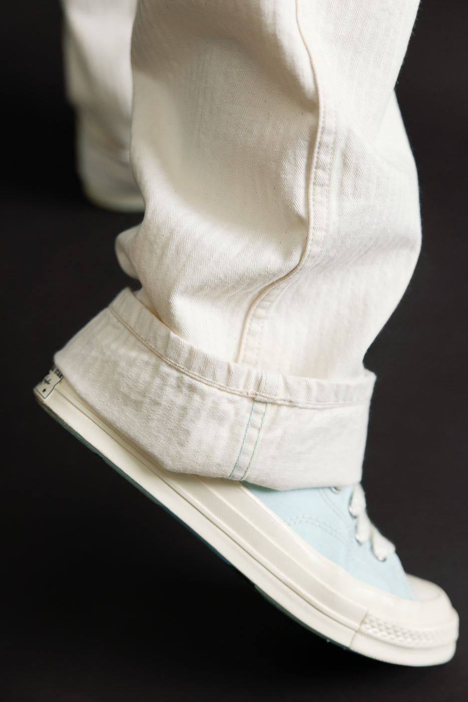 Close-up of lower leg and hem of natural white pants, side view, showing cuff detail and sneaker.