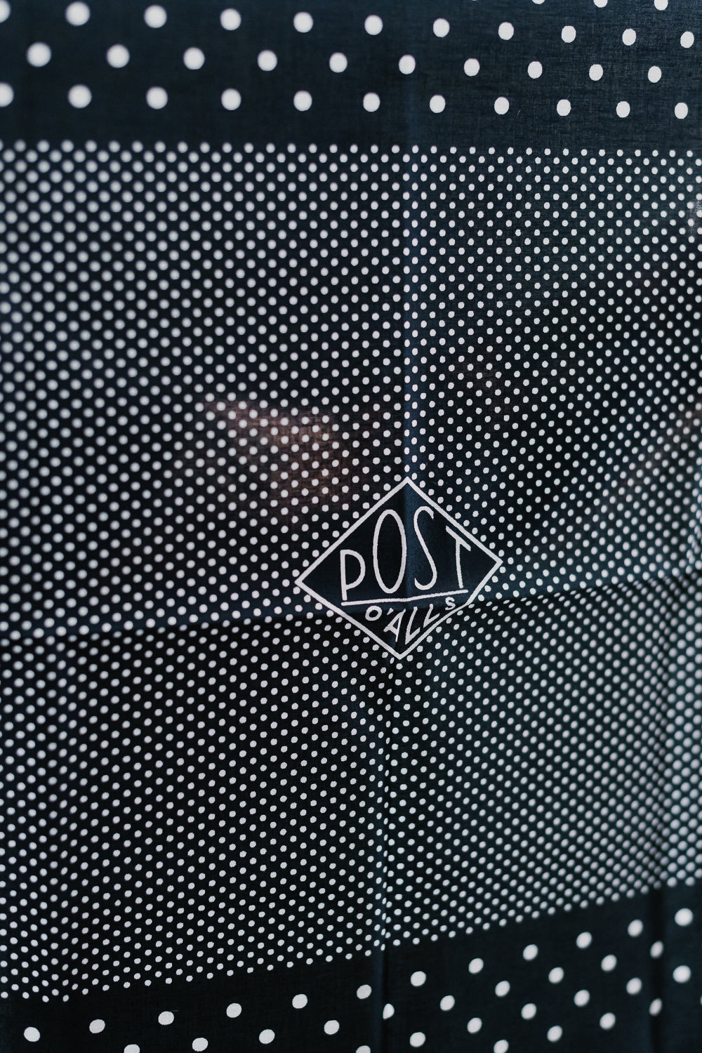 Close-up of Post O'Alls navy bandana scarf front, white polka dots, diamond logo detail