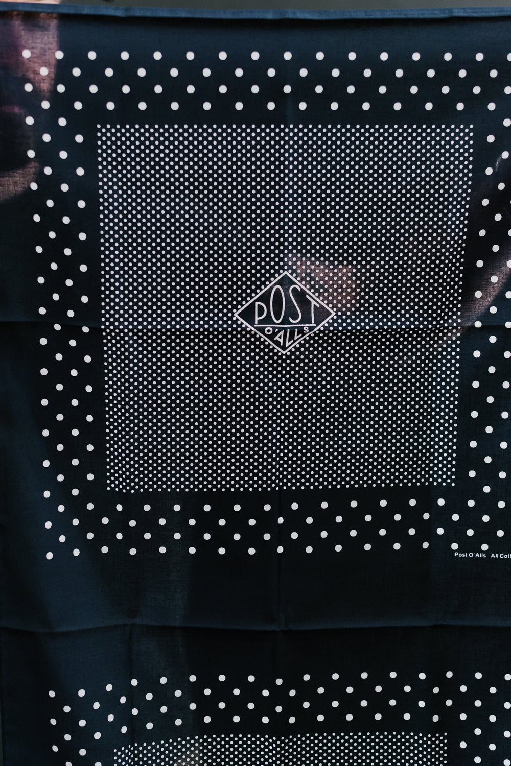 Close-up front view of Post O’Alls navy bandana scarf with white dot pattern, flat lay.