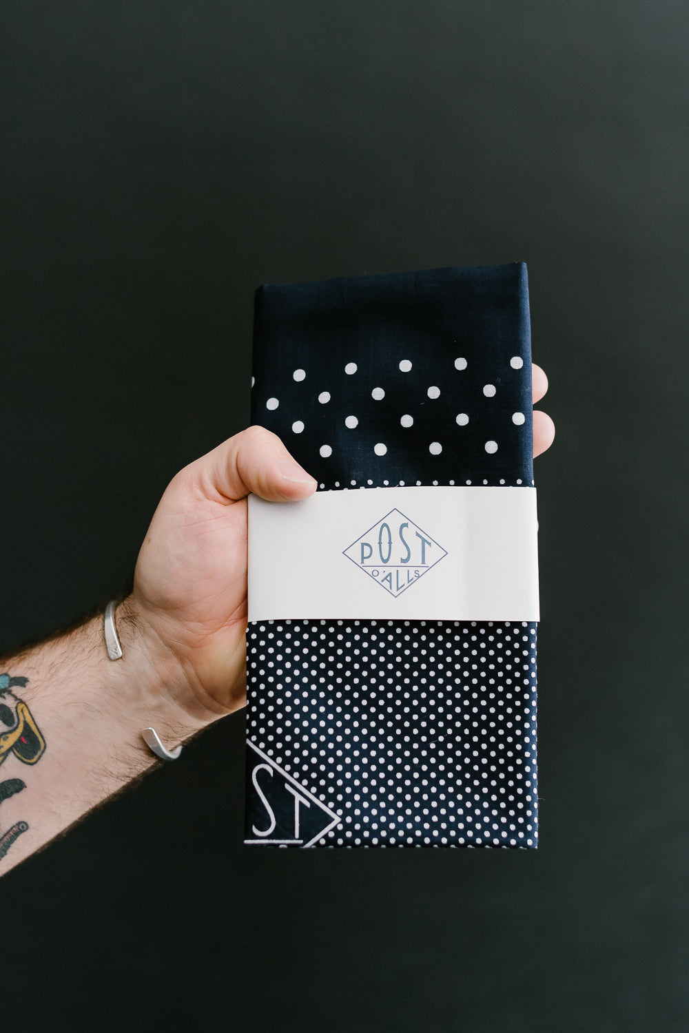 Close-up of navy Post O’Alls bandana scarf with white polka dots, front side, in hand.
