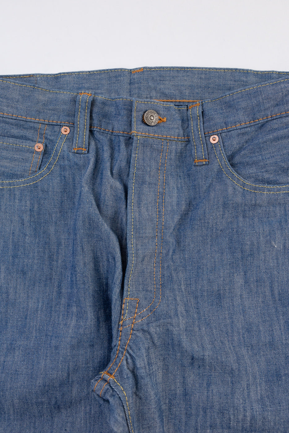 Close-up front view of blue denim jeans showing waist, button, and orange stitching details.
