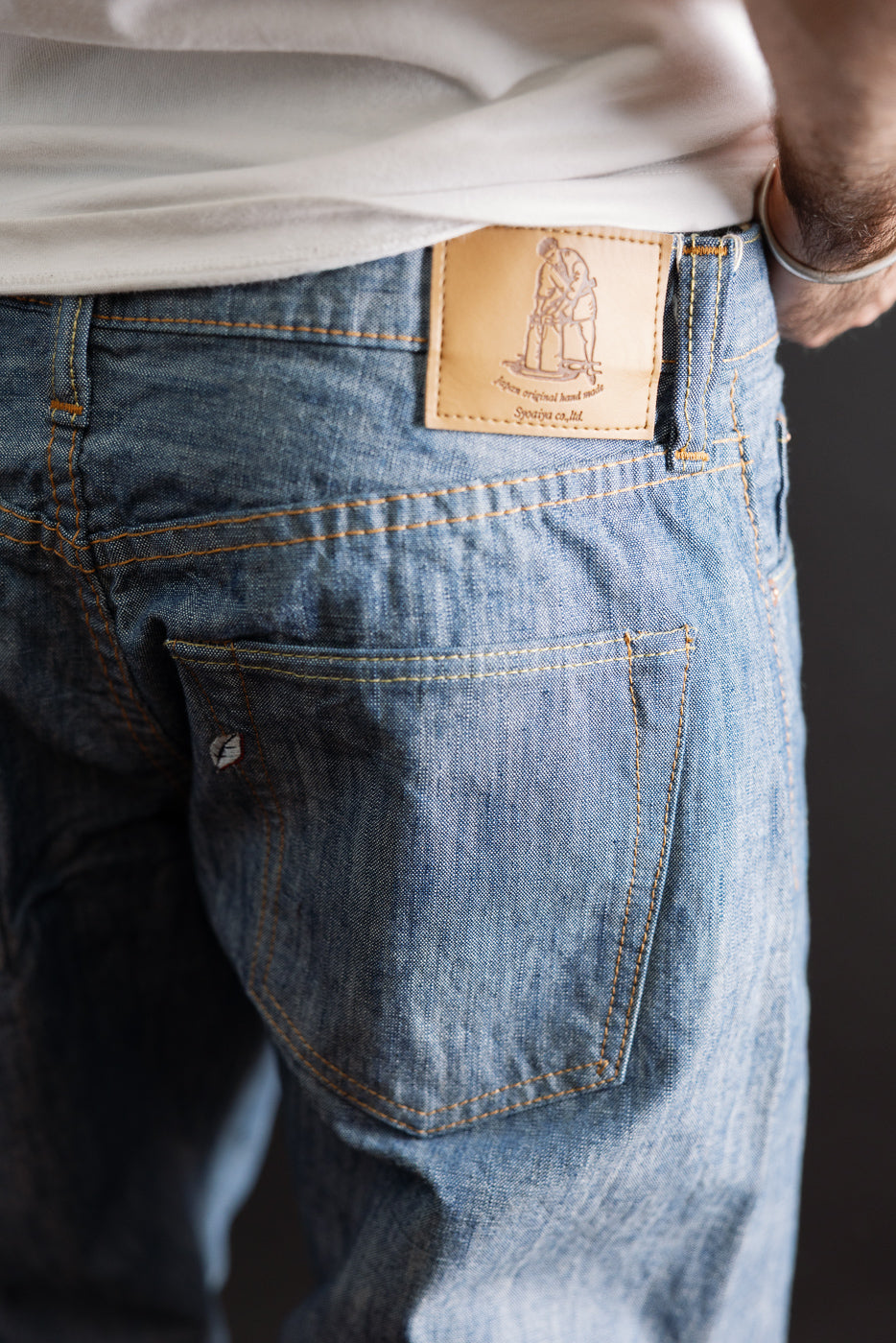 Close-up back view of light wash denim jeans featuring a leather waist patch and rear pocket detail.