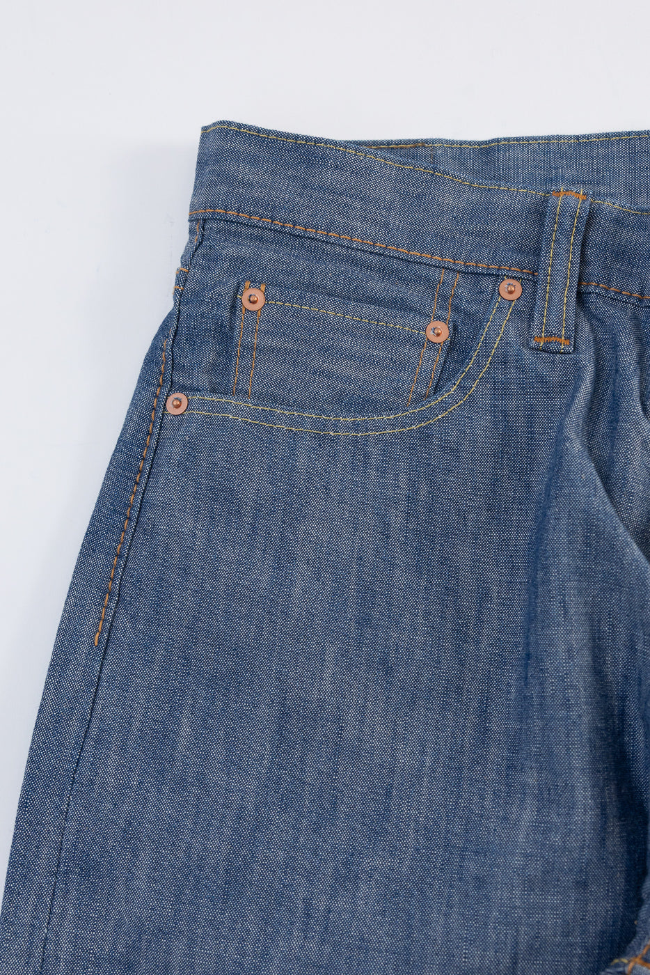 Close-up of the front right pocket and waistband of blue denim jeans with orange stitching.