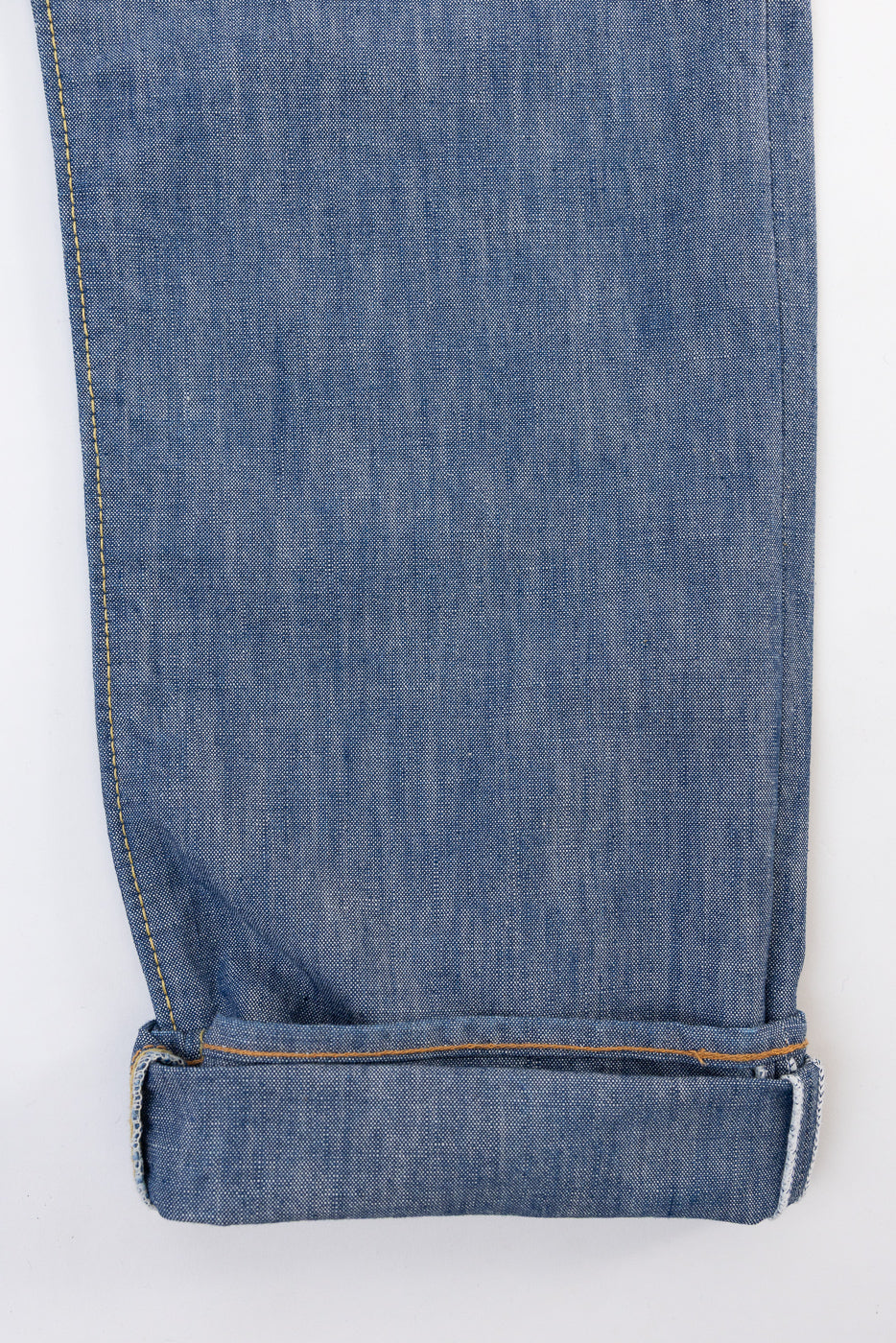 Close-up of the bottom hem and cuff of blue denim jeans showing fabric texture and gold stitching.