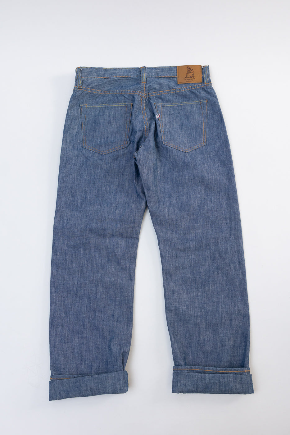 Back view flat lay of blue denim jeans with leather patch and cuffed hems.
