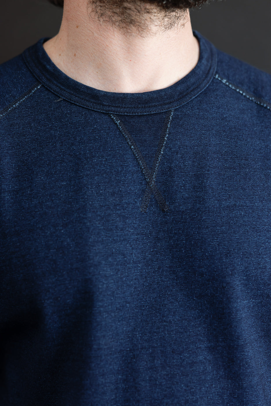 Close-up front view of male model wearing dark indigo raglan sweatshirt, showcasing ribbed crew neck and textured fabric.