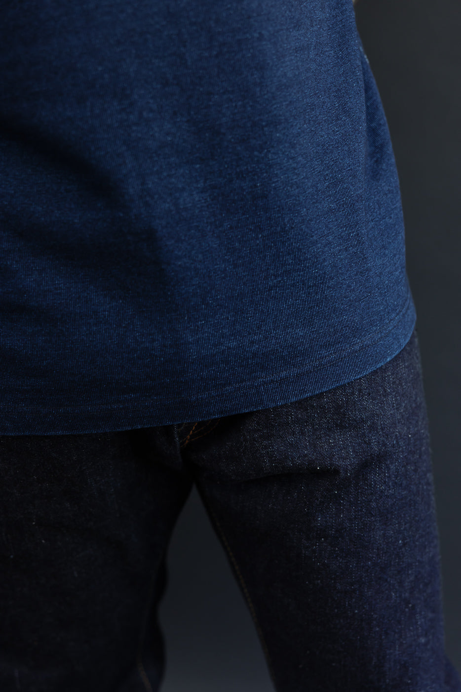 Close-up of male model's side, showcasing dark blue t-shirt hem and selvedge denim texture.