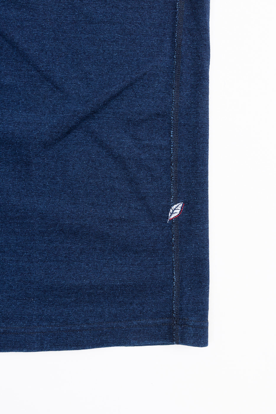 Close-up of navy blue t-shirt hem with leaf embroidery, showing side seam and fabric texture
