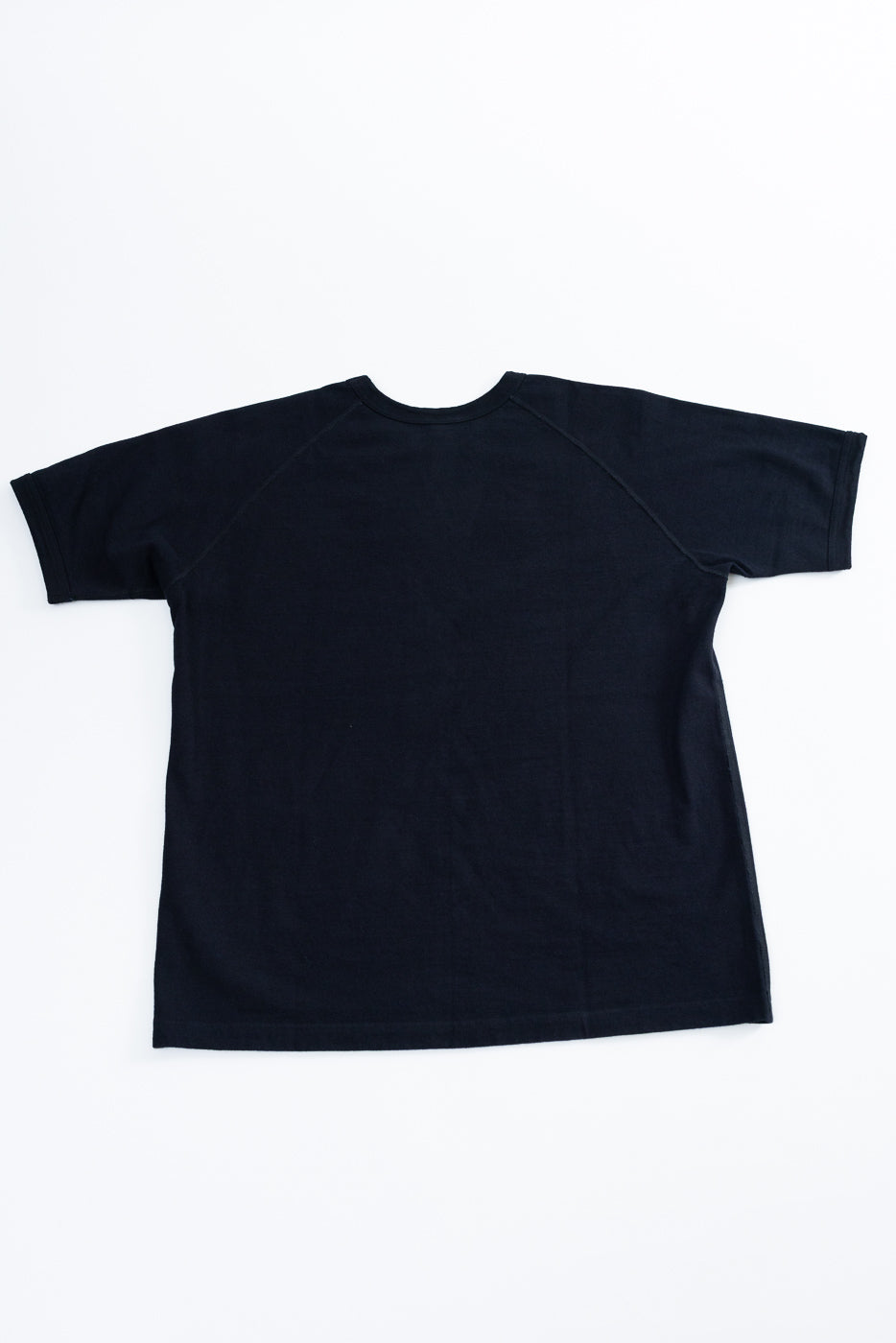 Flat lay back view of black raglan sleeve tee, showing crew neck and hem detail