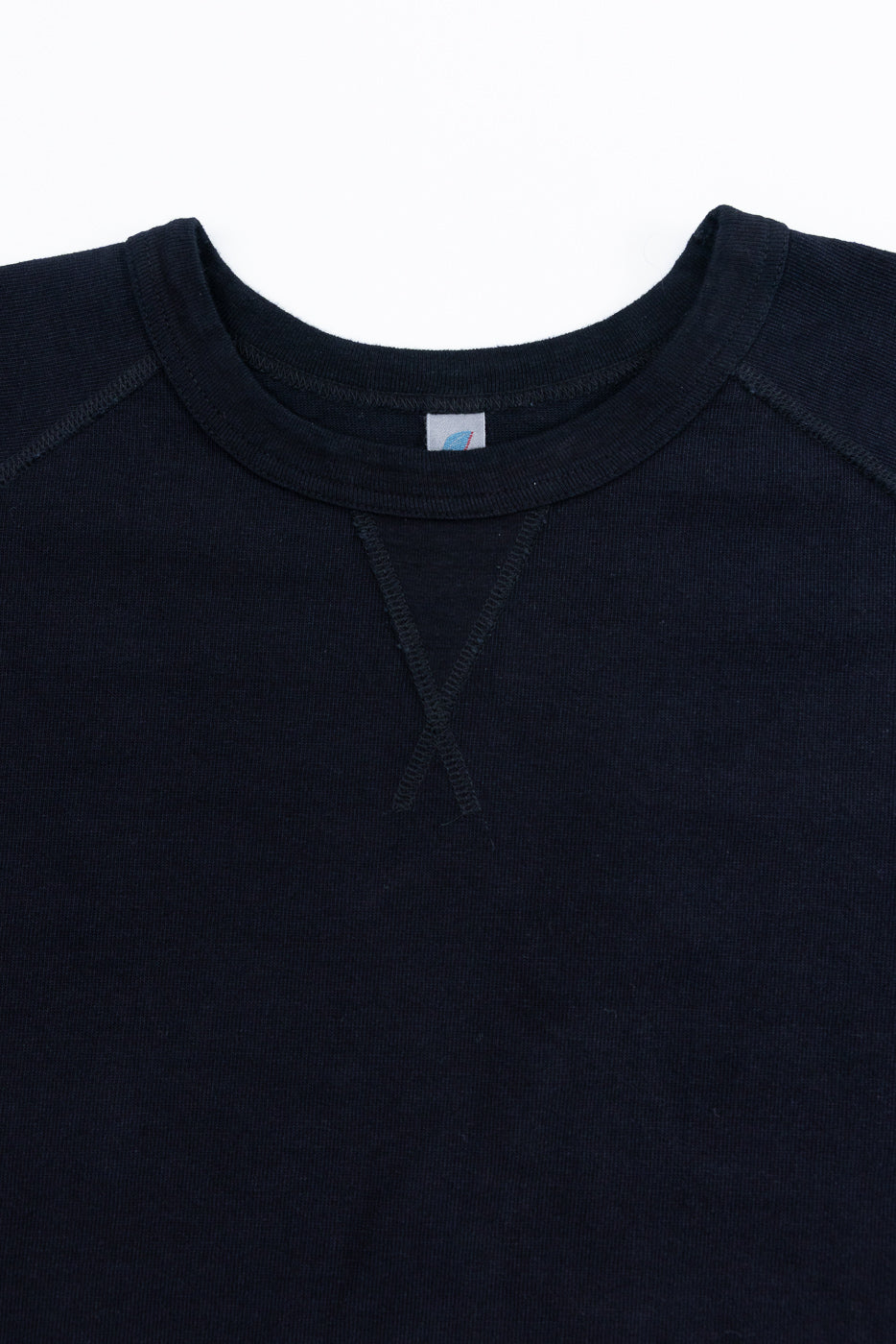Close-up front view of navy crewneck sweatshirt showing ribbed collar, tag, and V-stitch detail.