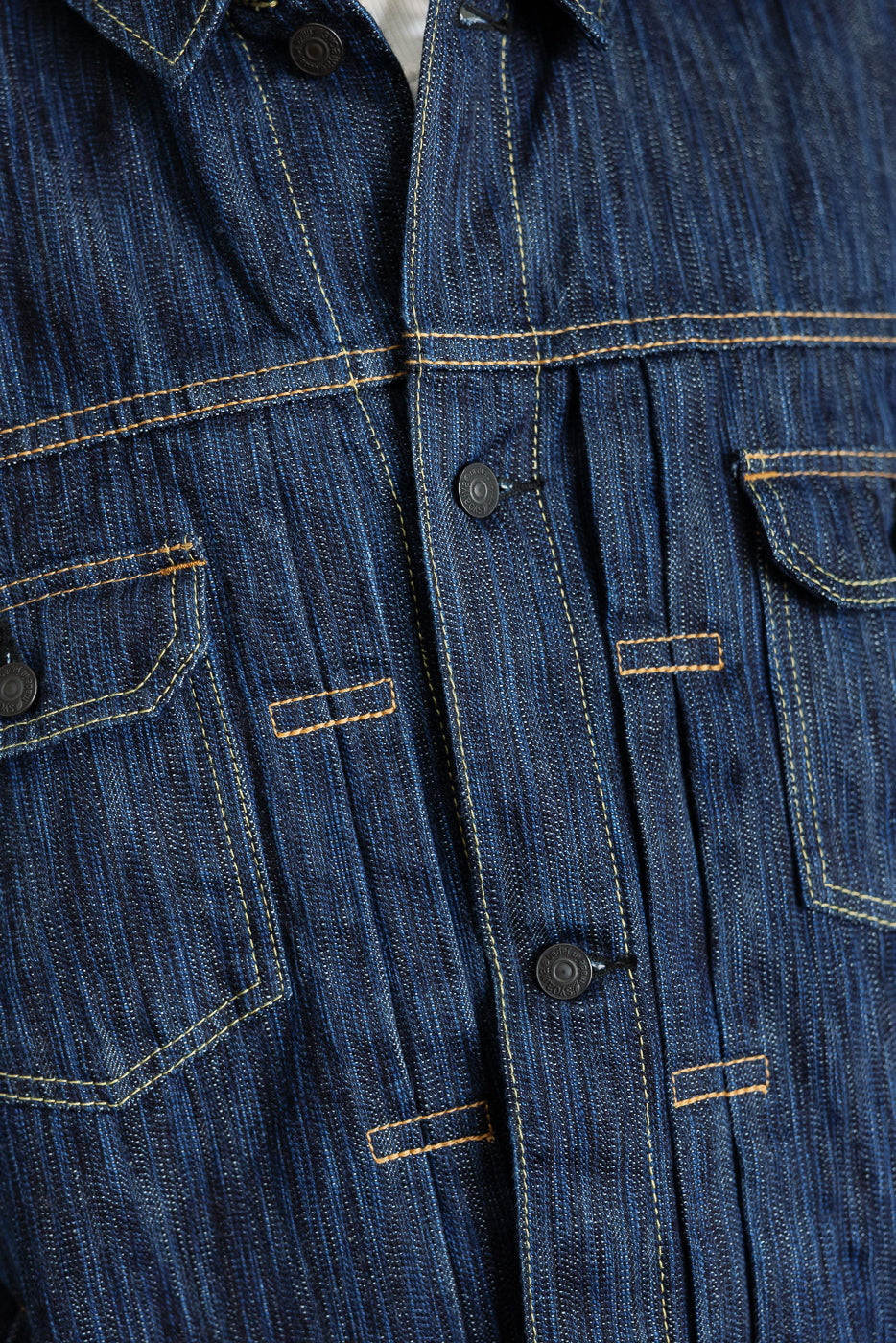 Close-up of the 6225-D Dark Waterfall Selvedge Type 2 Jacket featuring vertical-stripe denim weave, contrast yellow topstitching, flap chest pockets, and metal snap-style buttons on the front panel.