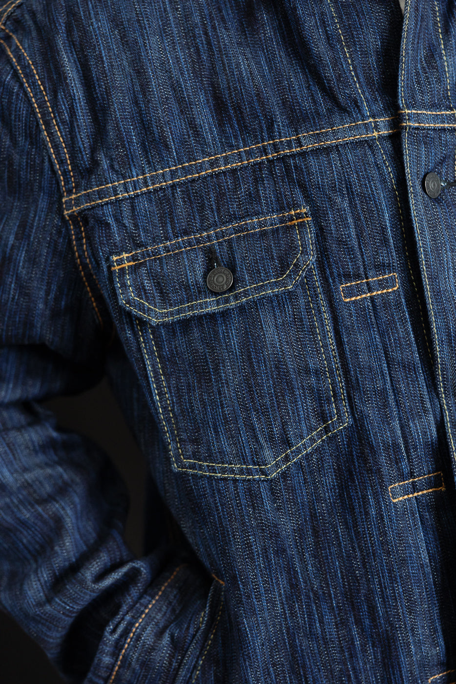 Close-up of the 6225-D - 14.5oz Dark Waterfall Selvedge Type 2 Jacket, showcasing a dark blue striped denim with contrast stitching, a flap chest pocket, and part of the wearer's arm.