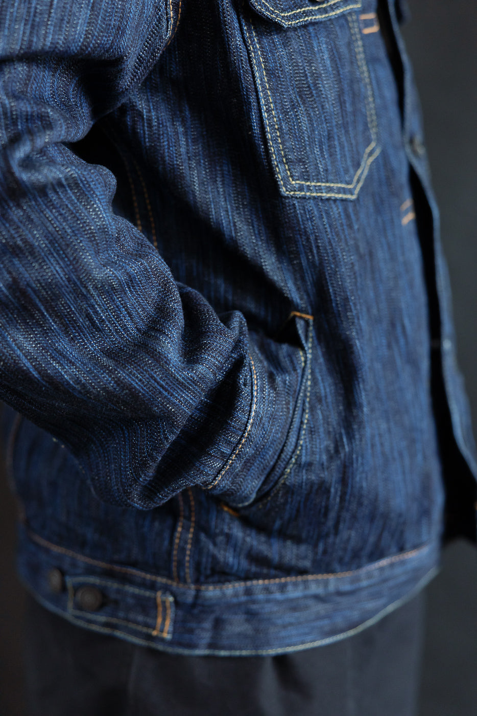 Close-up of the 6225-D Dark Waterfall Selvedge Type 2 Jacket, showcasing textured indigo denim with contrast stitching, flap chest pocket, and hand tucked in a side pocket, highlighting its intricate craftsmanship.