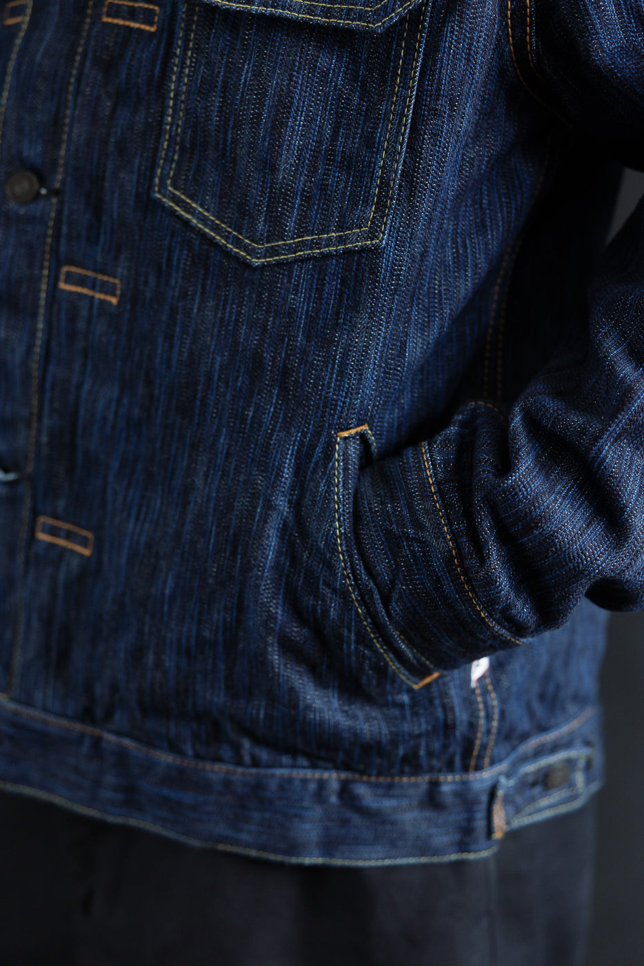 Close-up of the 6225-D - 14.5oz Dark Waterfall Selvedge Type 2 Jacket in indigo, showcasing the textured denim, contrast stitching, front placket, and welted hand-warmer pocket with a hand tucked in.