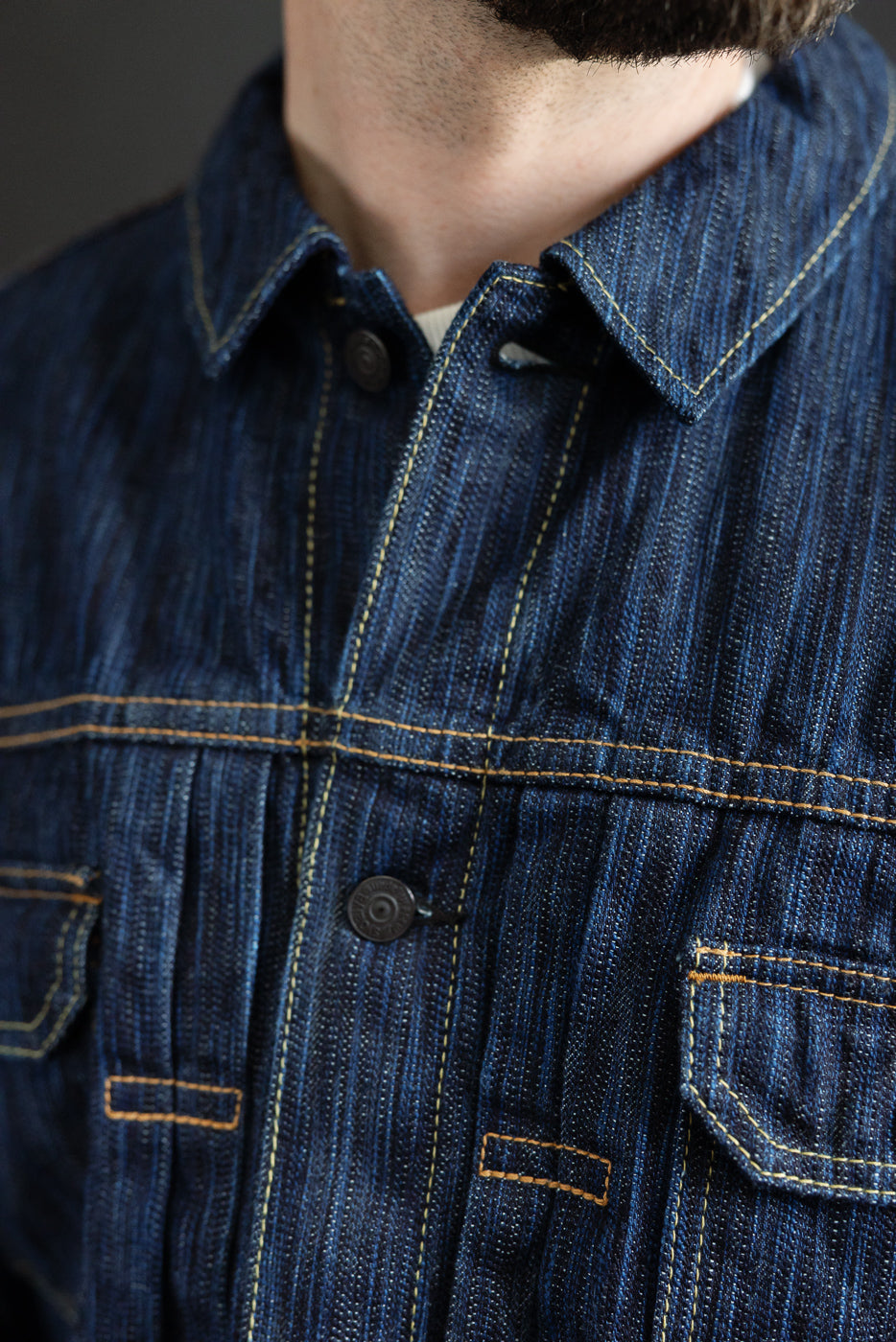 Dark Waterfall Selvedge Type 2 Jacket in Indigo, showcasing a pointed collar, contrast yellow stitching, metal chest button, and part of a flap pocket, highlighting detailed Japanese denim craftsmanship.