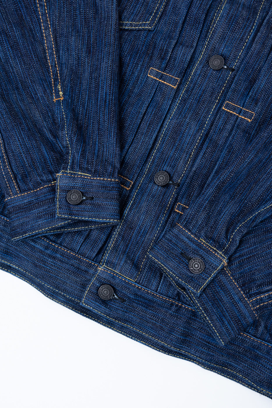 Close-up of the 6225-D - 14.5oz Dark Waterfall Selvedge Type 2 Jacket - Indigo, showcasing the indigo-dyed twill fabric, contrasting topstitching, and metal snap-buttons on the lower front and sleeve cuff.