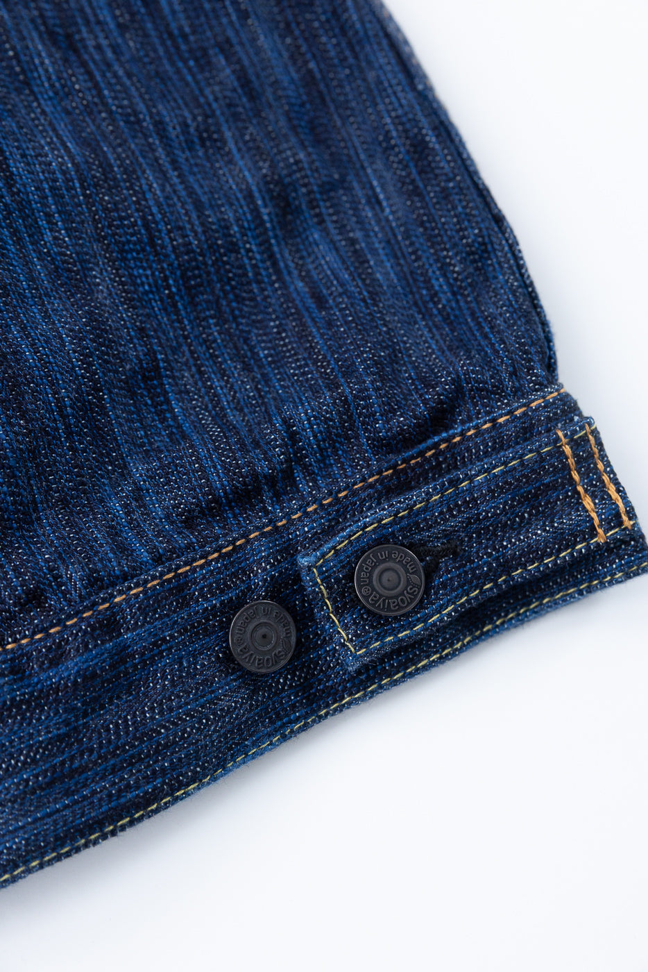 Close-up of the 6225-D - 14.5oz Dark Waterfall Selvedge Type 2 Jacket's waistband, featuring black metal snap buttons, yellow topstitching, and the textured slub surface of heavyweight Japanese selvedge denim.