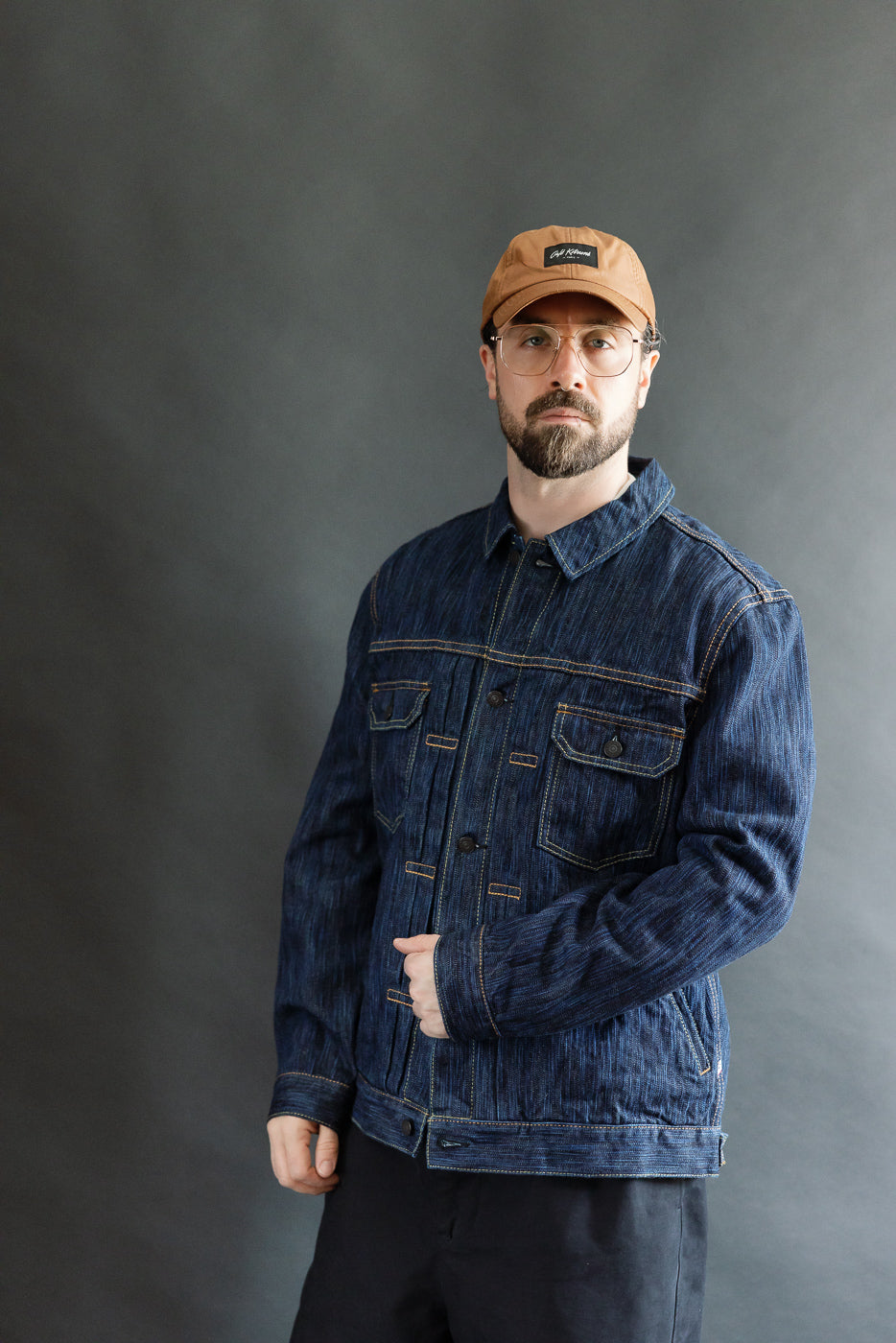 Bearded man models the 6225-D - 14.5oz Dark Waterfall Selvedge Type 2 Jacket - Indigo, showcasing contrast stitching, buttoned chest pockets, and a streamlined fit against a neutral-gray backdrop.