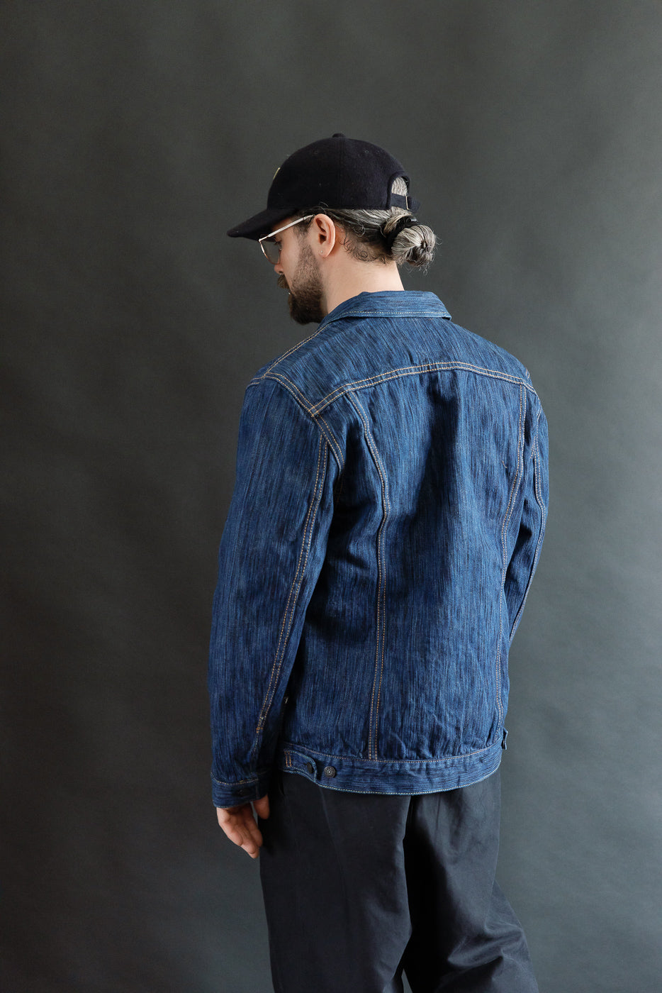 A person models the 6225-L - 14.5oz Light Waterfall Selvedge Type II Jacket, showcasing its indigo denim texture and Type-II silhouette with chest and hand-warmer pockets, against a dark background.