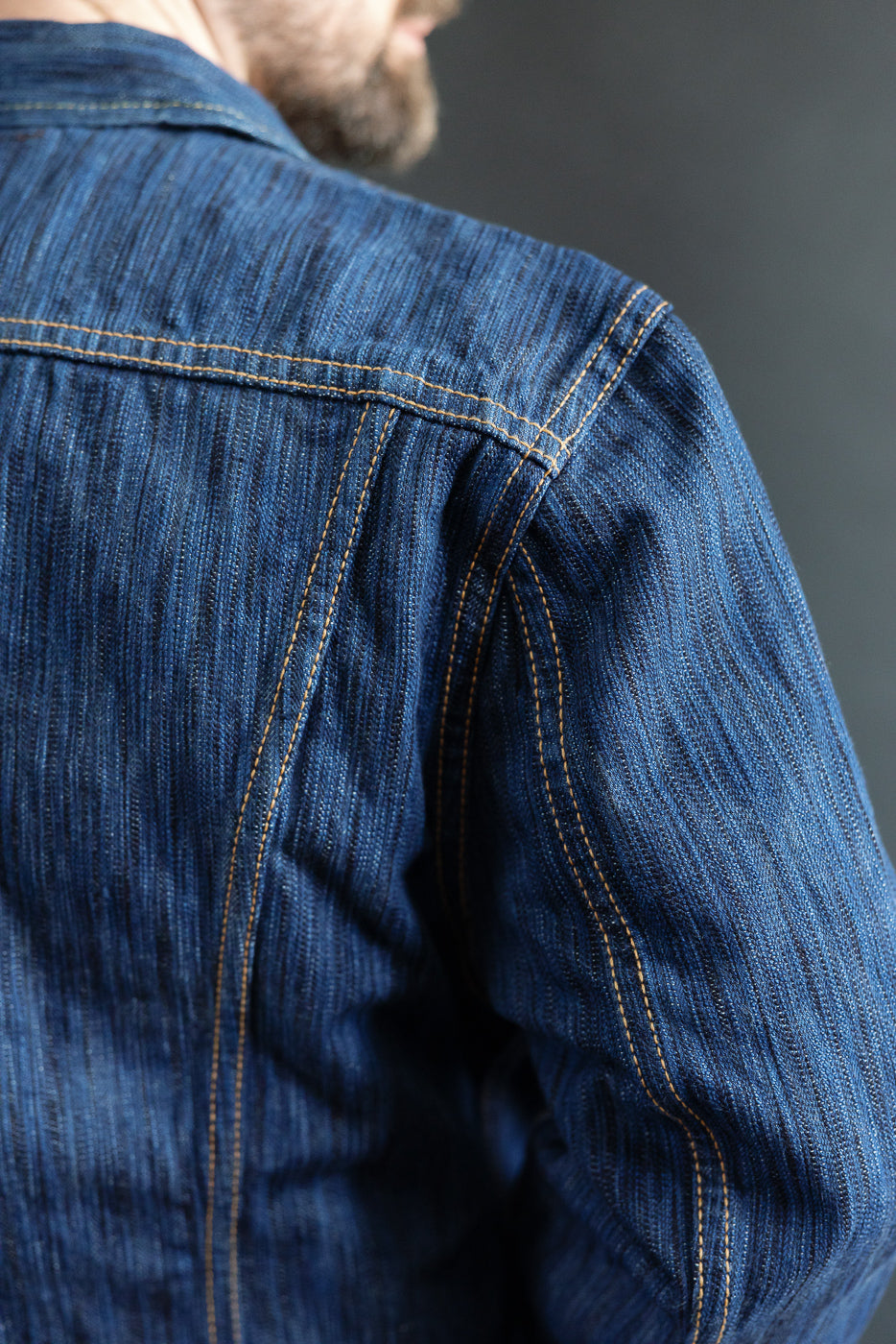 Close-up of the 6225-L - 14.5oz Light Waterfall Selvedge Type II Jacket in indigo, highlighting the blue denim texture, golden stitching, and a hint of the wearer's beard and jawline.