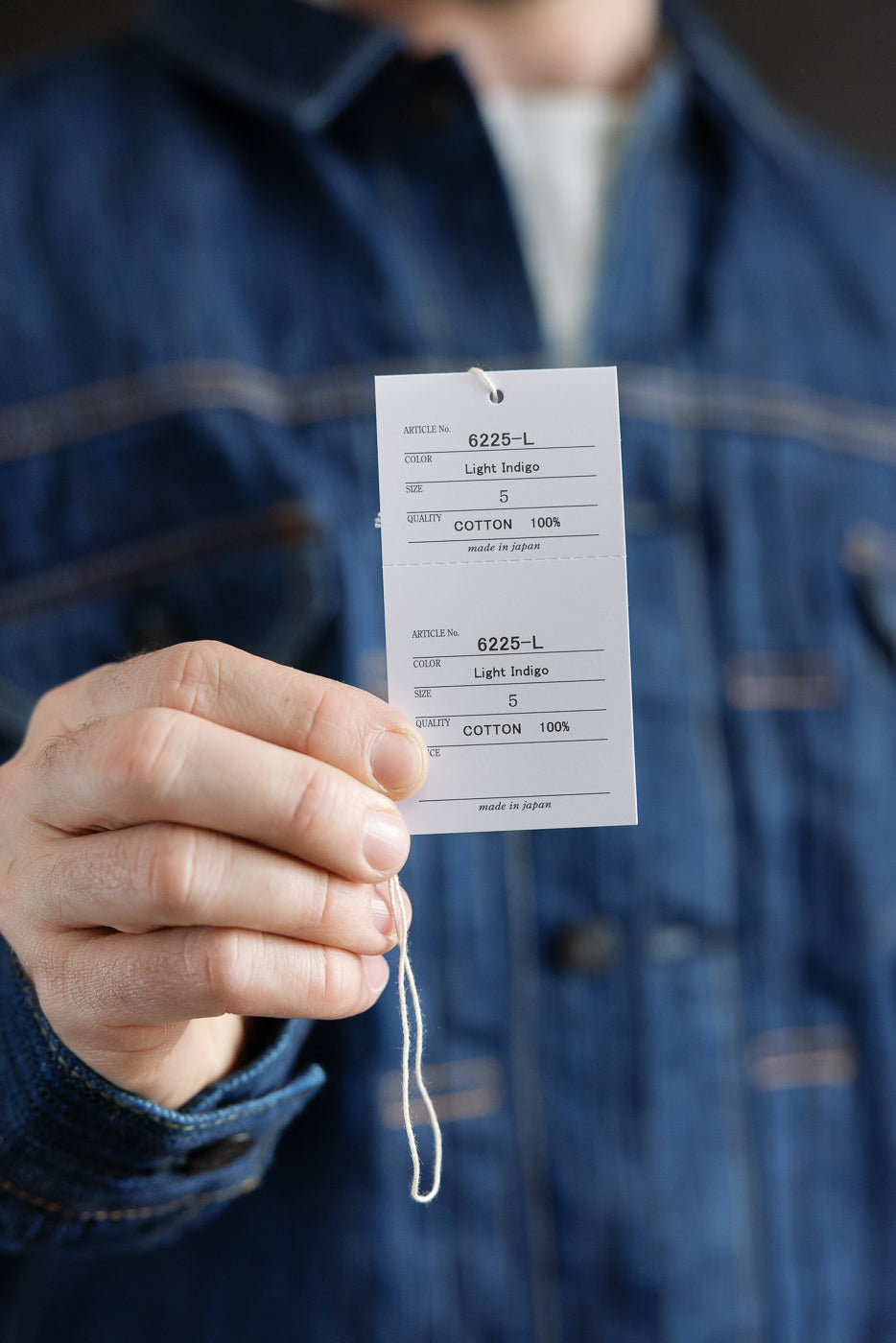 A close-up of a denim jacket's hang-tags, detailing the 6225-L - 14.5oz Light Waterfall Selvedge Type II Jacket - Indigo, highlighting its Japanese craftsmanship and unique textured slub denim.