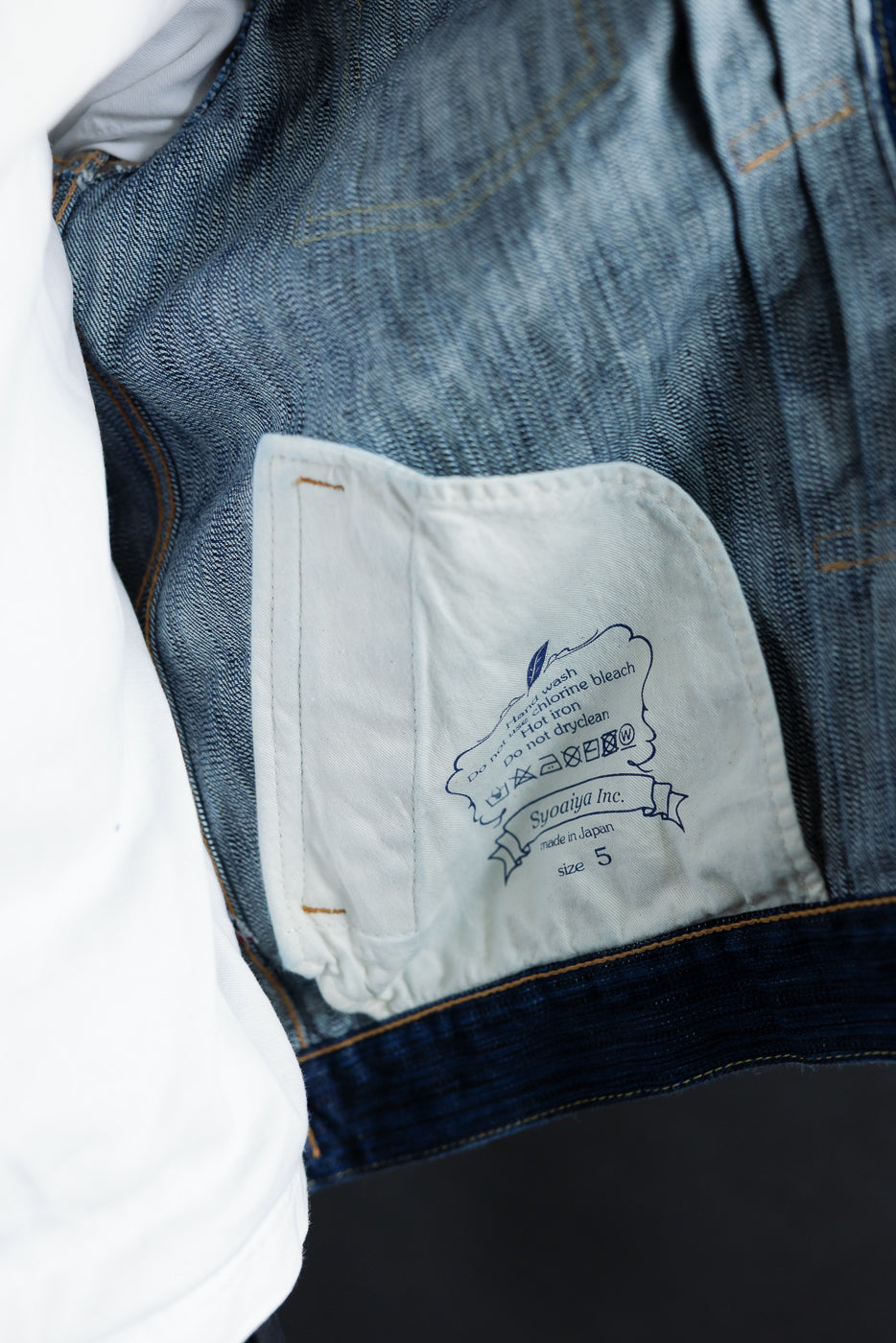 Close-up of 6225-L - 14.5oz Light Waterfall Selvedge Type II Jacket, showcasing the inside pocket with care label, indigo weave, and orange top-stitching, reflecting its artisanal Japanese construction.