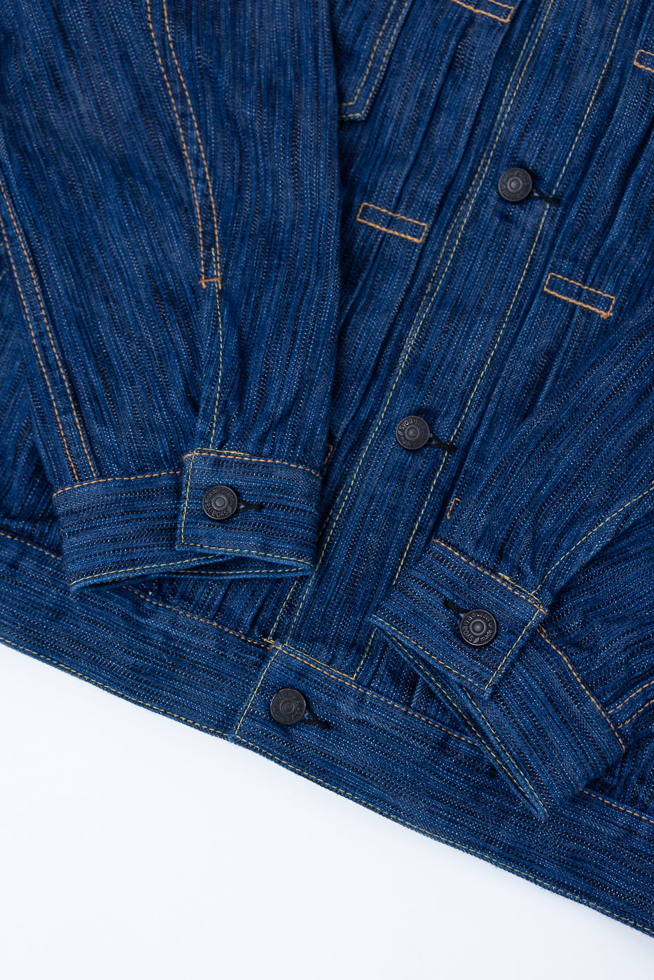 Close-up of the 6225-L - 14.5oz Light Waterfall Selvedge Type II Jacket, showcasing indigo denim with textured slub, yellow top-stitching, and matte black buttons on a flat layout, highlighting craftsmanship and detail.