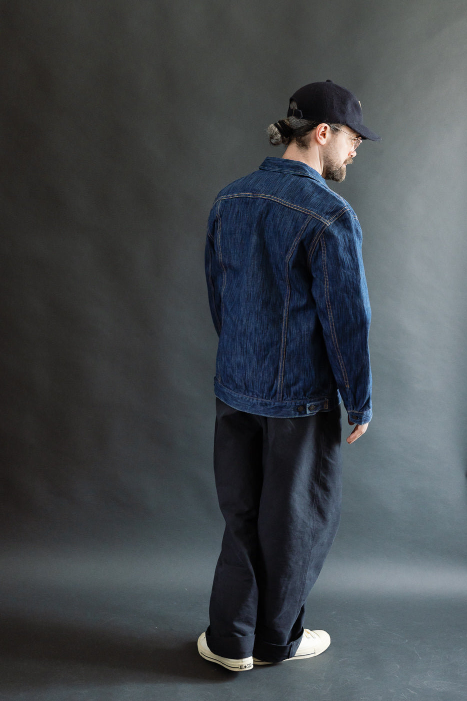 A man models the 6225-L - 14.5oz Light Waterfall Selvedge Type II Jacket in Indigo, showcasing the jacket's textured Japanese denim, chest pockets, and signature leaf embroidery, paired with black pants and off-white sneakers.