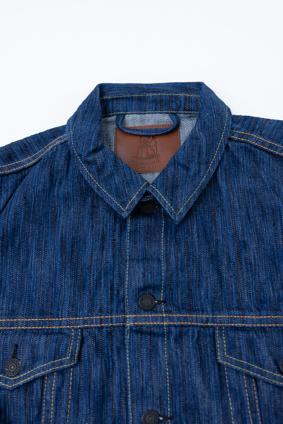 Close-up of the 6226-L - 14.5oz Light Waterfall Selvedge Type III Jacket in Indigo, showcasing its slub texture, folded collar, button-front, contrast-stitched chest pockets, and interior leather brand patch.