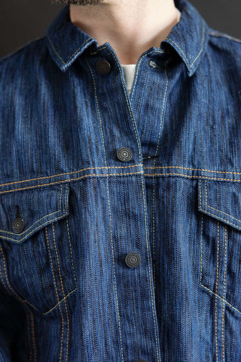 Close-up of the Light Waterfall Selvedge Type III Jacket in indigo, showcasing pointed flap chest pockets, metal snap buttons, and subtle vertical stripe texture, embodying Pure Blue Japan's signature denim craftsmanship.