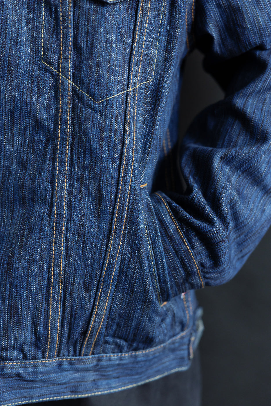 Close-up of the 6226-L - 14.5oz Light Waterfall Selvedge Type III Jacket - Indigo, showcasing contrast stitching, selvedge detailing, and a hand in a welted side pocket on textured Japanese denim.