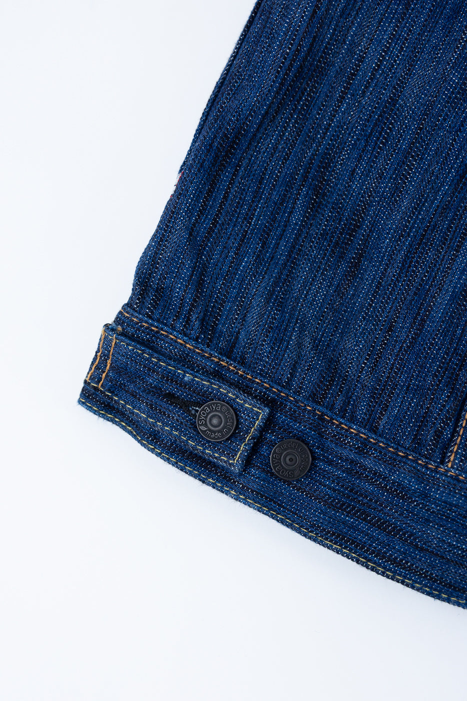 Close-up of the 6226-L - 14.5oz 'Light Waterfall' Selvedge Type III Jacket - Indigo hem, showing blue denim fabric, yellow-orange stitching, and adjustable side tab with metal snap buttons.