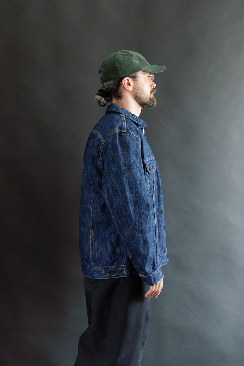 Man wearing 6226-L - 14.5oz Light Waterfall Selvedge Type III Jacket - Indigo in profile, showcasing the denim's slub texture, knife pleats, pointed flap pockets, and chainstitch details, embodying Dant's premium menswear style.