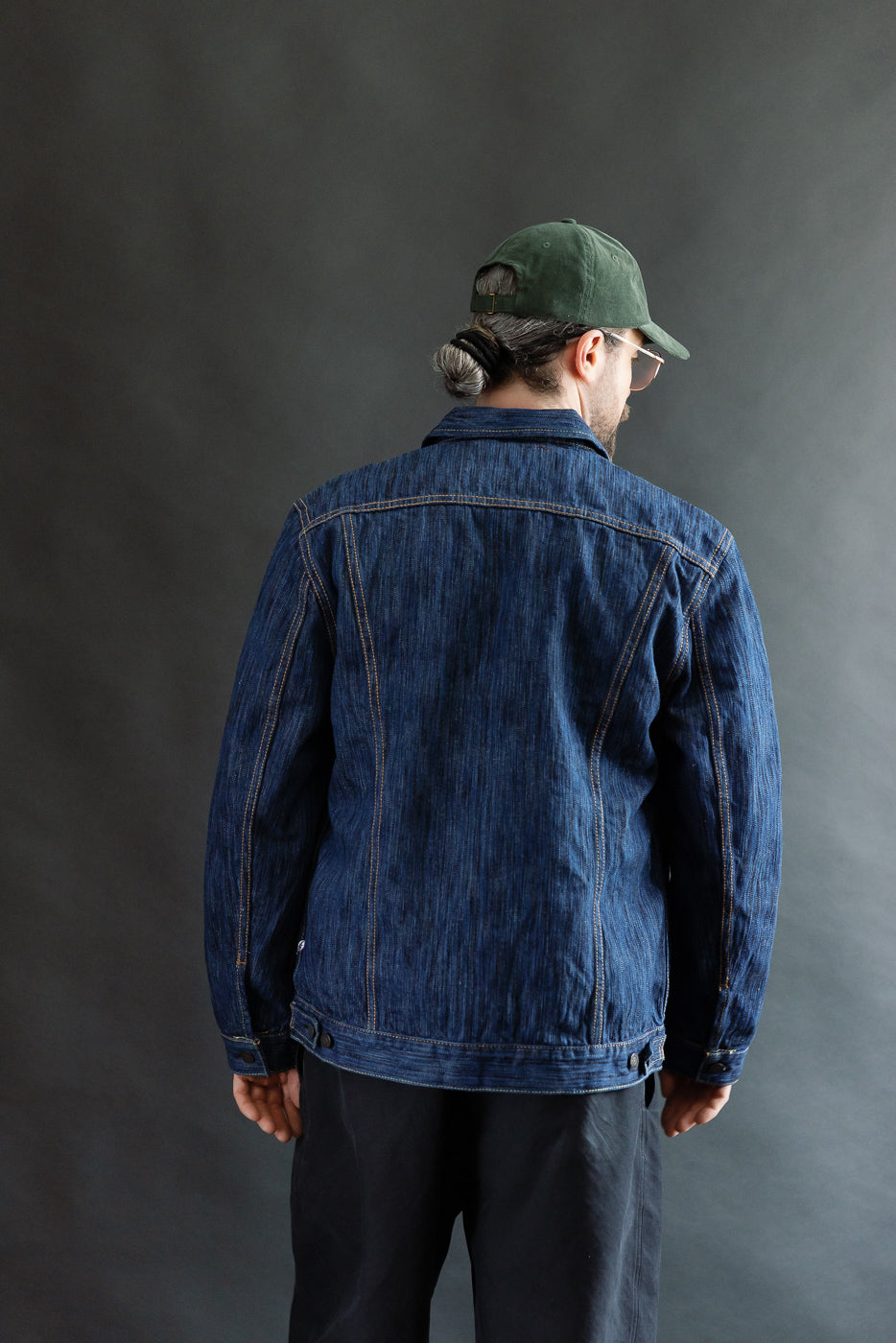 Person wearing the 6226-L - 14.5oz Light Waterfall Selvedge Type III Jacket - Indigo, showcasing its structured silhouette and signature details like knife pleats and pointed flap pockets, against a dark gray backdrop.