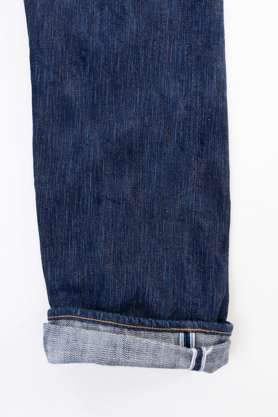 Flat lay, close-up of the bottom hem and selvedge detail of dark indigo denim jeans.