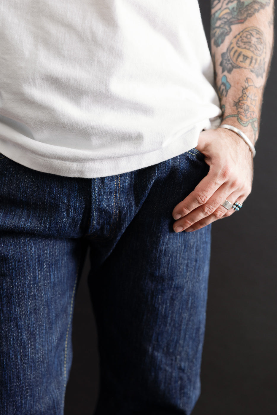 Close-up of the front waist and pocket of dark indigo selvedge denim jeans on a male model.