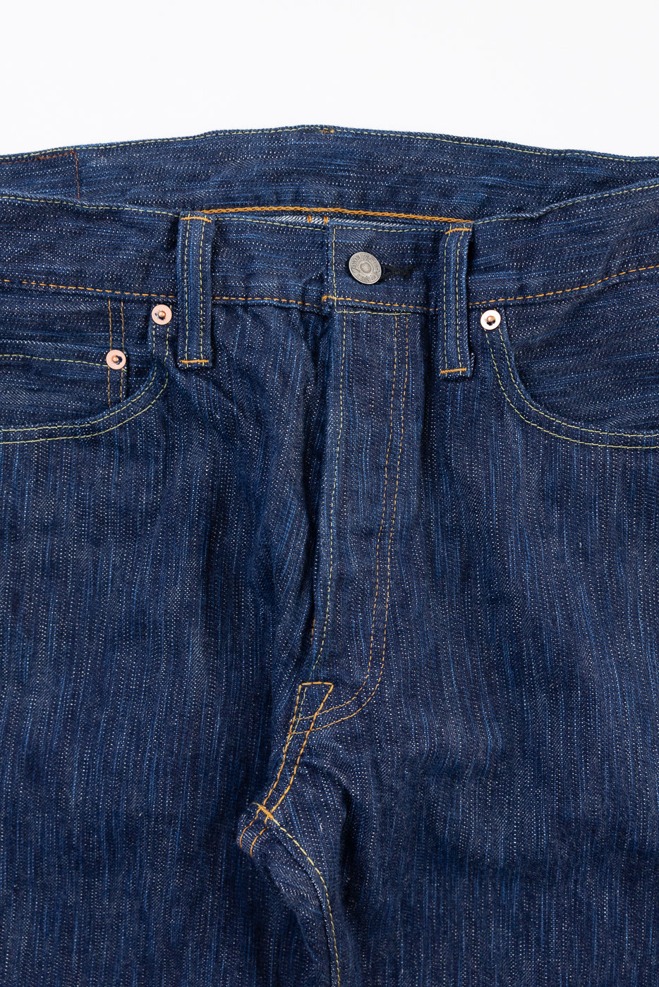 Front view close-up of dark indigo selvedge denim jeans showing waistband, button, and fly.