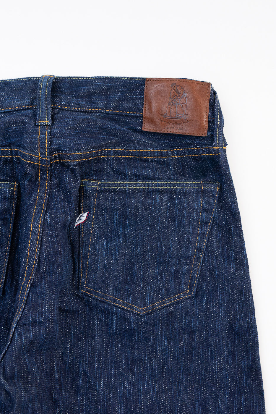 Close-up back view of dark indigo selvedge denim jeans showing rear pocket and leather patch.