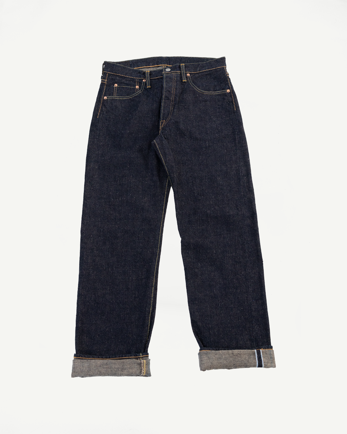 Front view flat lay of dark indigo selvedge denim jeans with cuffed hems.