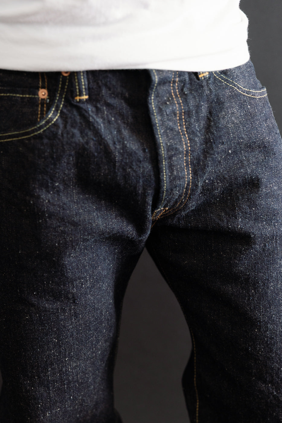 Close-up of the front waist and crotch area of dark indigo selvedge denim jeans on a male model.